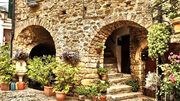 Un bâtiment en pierre doté de deux portes en arc de cercle, entouré de plantes en pot et dont le sol est pavé de pierres.