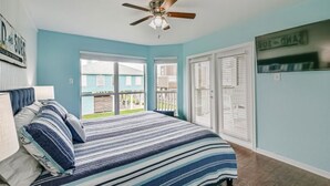A bedroom with a bed, a ceiling fan, and a view of the outside. - OCEAN VIEWS! Steps away from the sand! (Galveston)