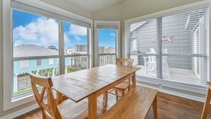 A dining area with a wooden table and chairs, large windows, and a view of a residential neighborhood. - OCEAN VIEWS! Steps away from the sand! (Galveston)