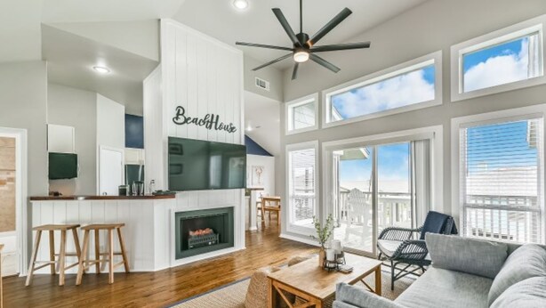 A spacious living area with a fireplace, a dining table, and a large window overlooking the city. - OCEAN VIEWS! Steps away from the sand! (Galveston)