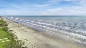A beach with a long stretch of sand, a few people, and a clear sky. - OCEAN VIEWS! Steps away from the sand! (Galveston)