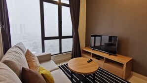 A modern living room with a sofa, a round coffee table, a TV on a wooden stand, and a large window with curtains. - OYO Home 90400 One Tebrau Homestay (Johor Bahru)