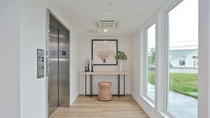 A modern elevator with a control panel, a framed artwork above it, a small table with candles and a plant, and a wicker basket on the floor. - Harbourtown Suites (Plymouth)