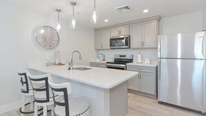 A modern kitchen with a central island, stainless steel appliances, pendant lighting, and a round wall clock. - Harbourtown Suites (Plymouth)