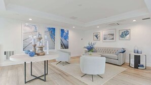 A modern living room with a round dining table, a sofa, and a coffee table. There are large windows with abstract art on the walls. - Harbourtown Suites (Plymouth)