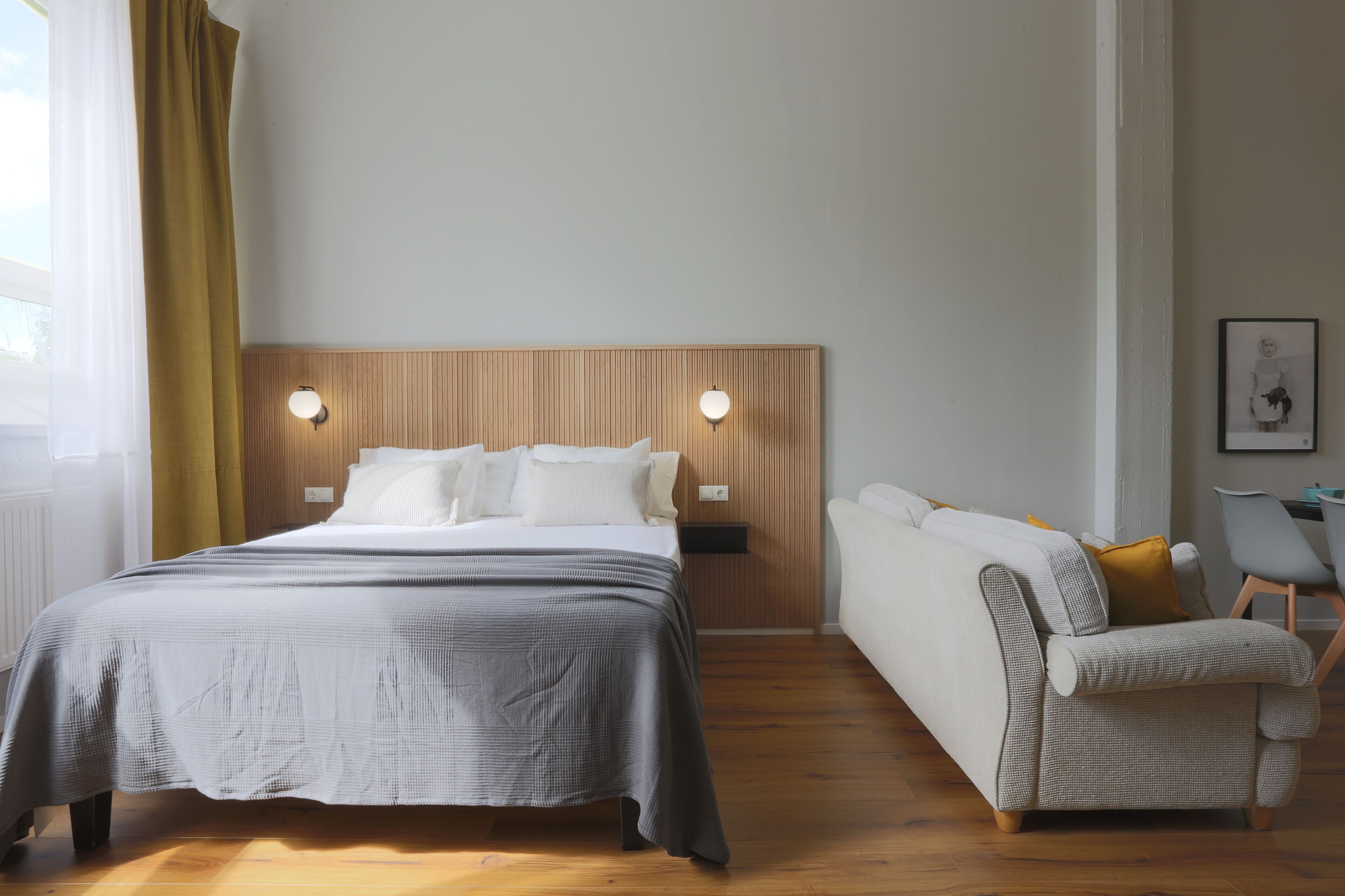 A modern hotel room with a bed, bedside tables, a sofa, and a chair.