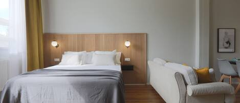 A modern hotel room with a bed, bedside tables, a sofa, and a chair.