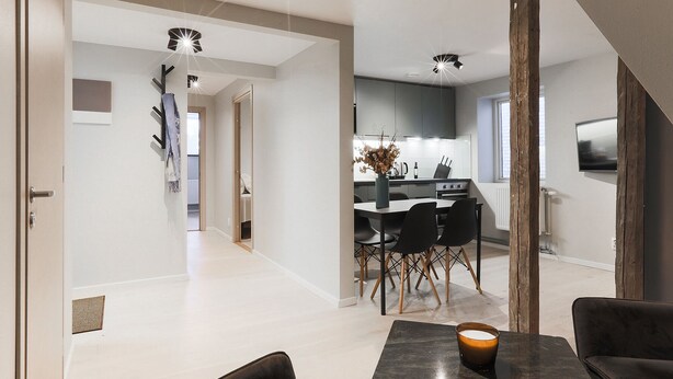 A modern kitchen with a dining area, featuring a central island, black chairs, and a vase with flowers. - Foundry Hotel Apartments (Uppsala)