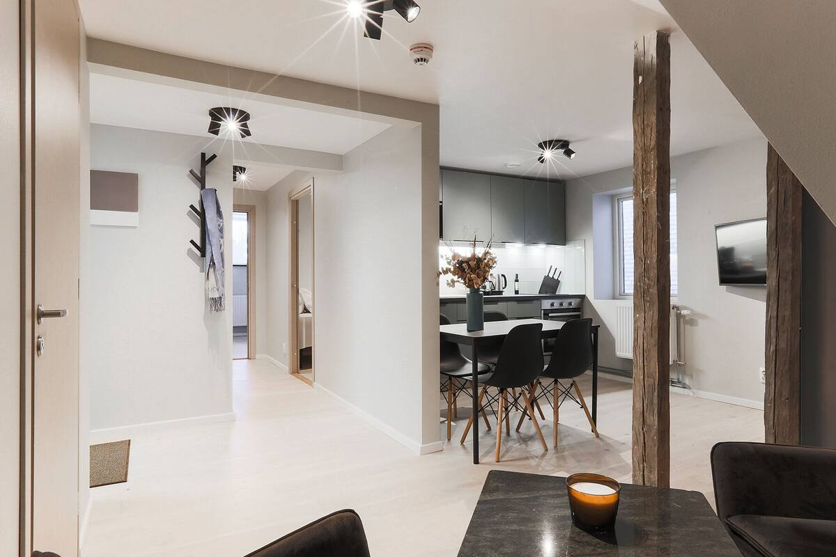A modern kitchen with a dining area, featuring a central island, black chairs, and a vase with flowers.
