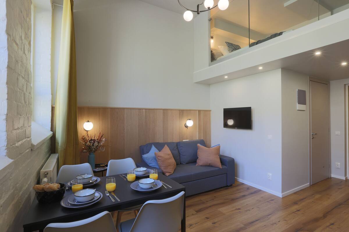 A modern dining area with a table set for breakfast, a sofa, and a staircase leading to an upper level.