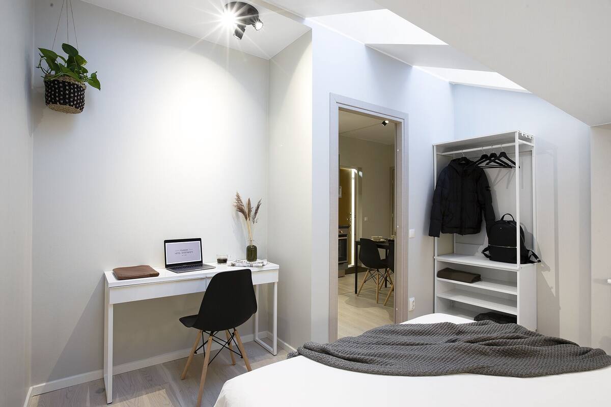 A modern bedroom with a skylight, a desk with a laptop, a chair, a bed, and a wardrobe.