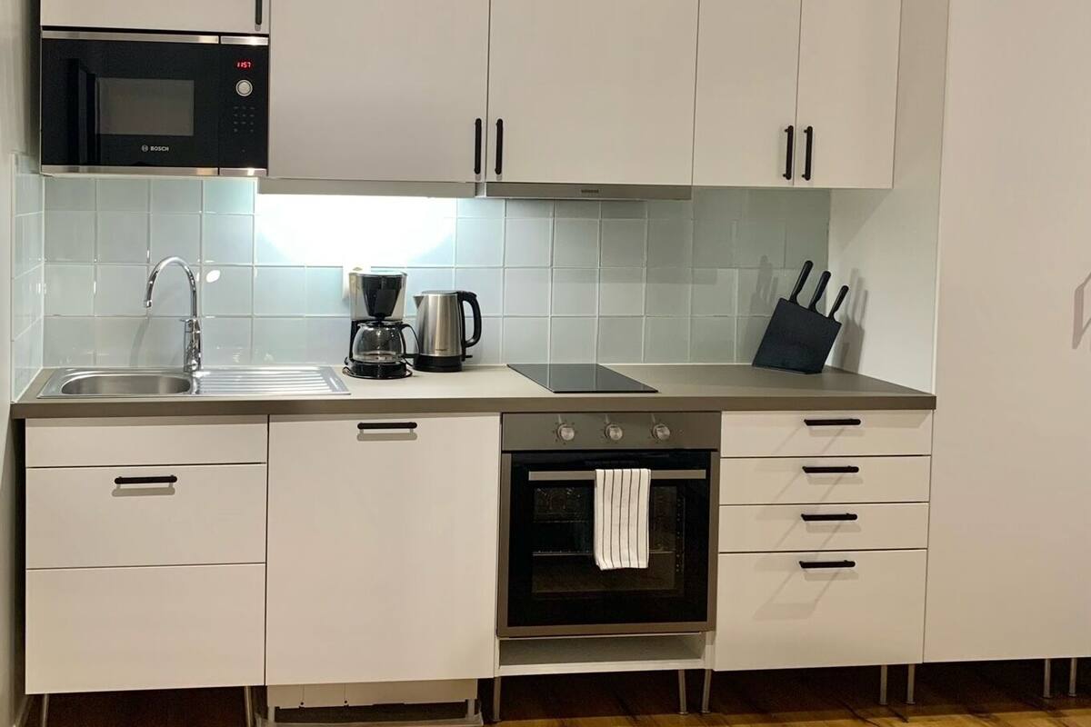 A modern kitchen with white cabinets, a Bosch microwave, a coffee maker, and a sink.