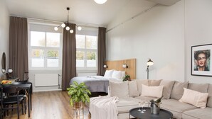 A modern bedroom with a bed, bedside table, and a large window with curtains. - Foundry Hotel Apartments (Uppsala)