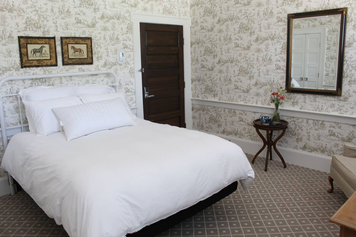 A bedroom with a bed, a door, a mirror, and two framed pictures on the wall.