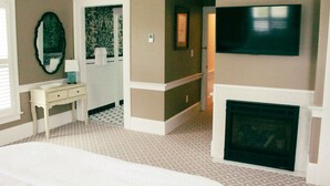 A hotel room with a bed, a television, a fireplace, a mirror, and a small table. - Inn at Mary's Land Farm (Clarksville)