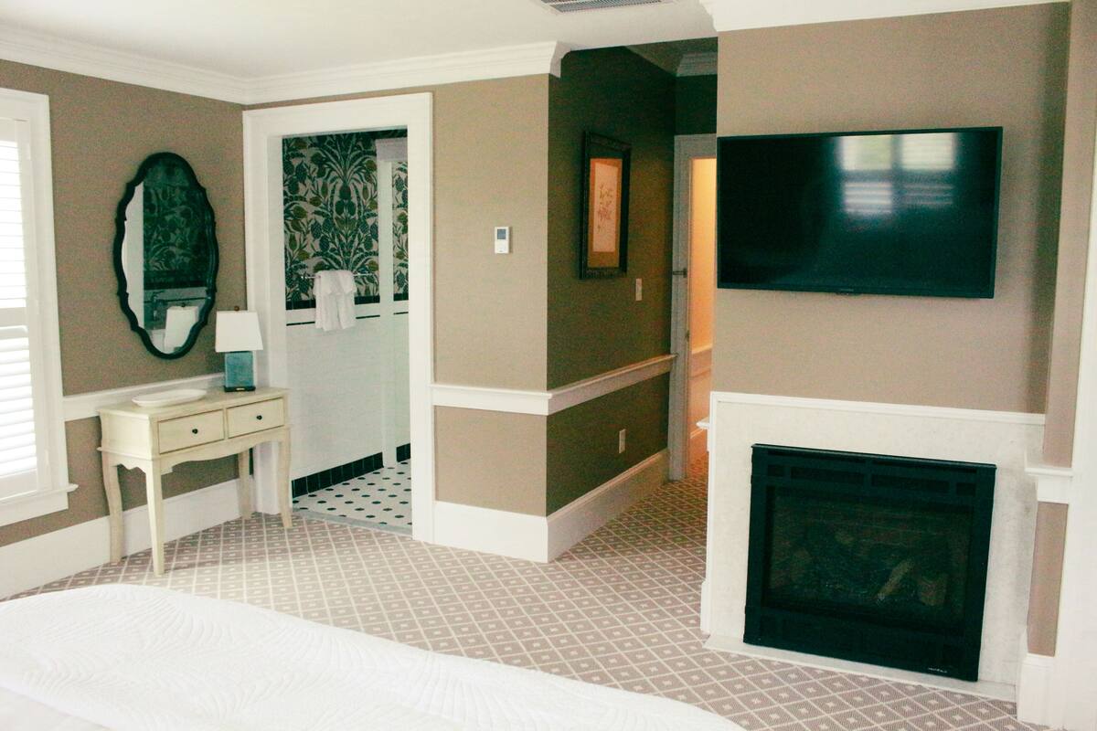 A hotel room with a bed, a television, a fireplace, a mirror, and a small table.