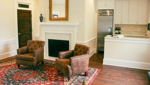 A living room with two armchairs, a fireplace, and a kitchen area with a refrigerator and wine bottles. - Inn at Mary's Land Farm (Clarksville)