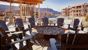 An outdoor seating area with Adirondack chairs and a fire pit, surrounded by buildings with balconies and a mountain view. - WorldMark Moab  (Moab)