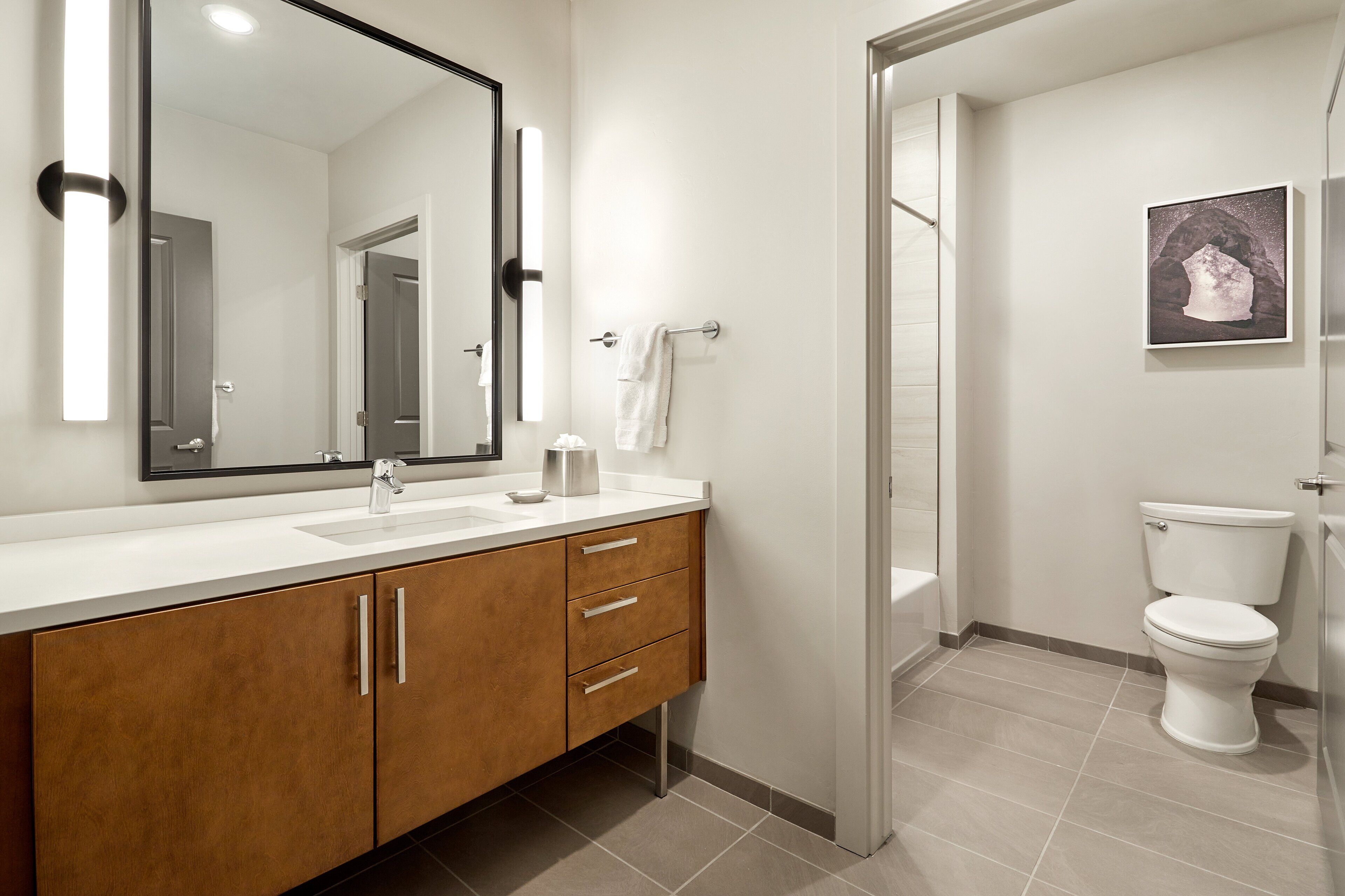 Un baño moderno con tocador de madera, un espejo grande, inodoro y zona de ducha.