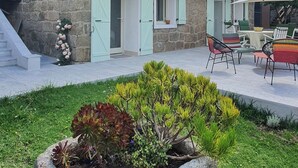 En bygning i sten med balkon, have med planter og udendørs møbler.