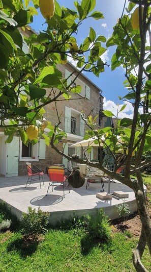 A courtyard with outdoor seating, a stone building with balconies, and a tree with fruit.
