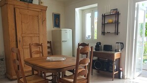 Et spiseområde med et træbord og stole, et køleskab, kaffemaskine og en hylde med stearinlys og en billedramme.