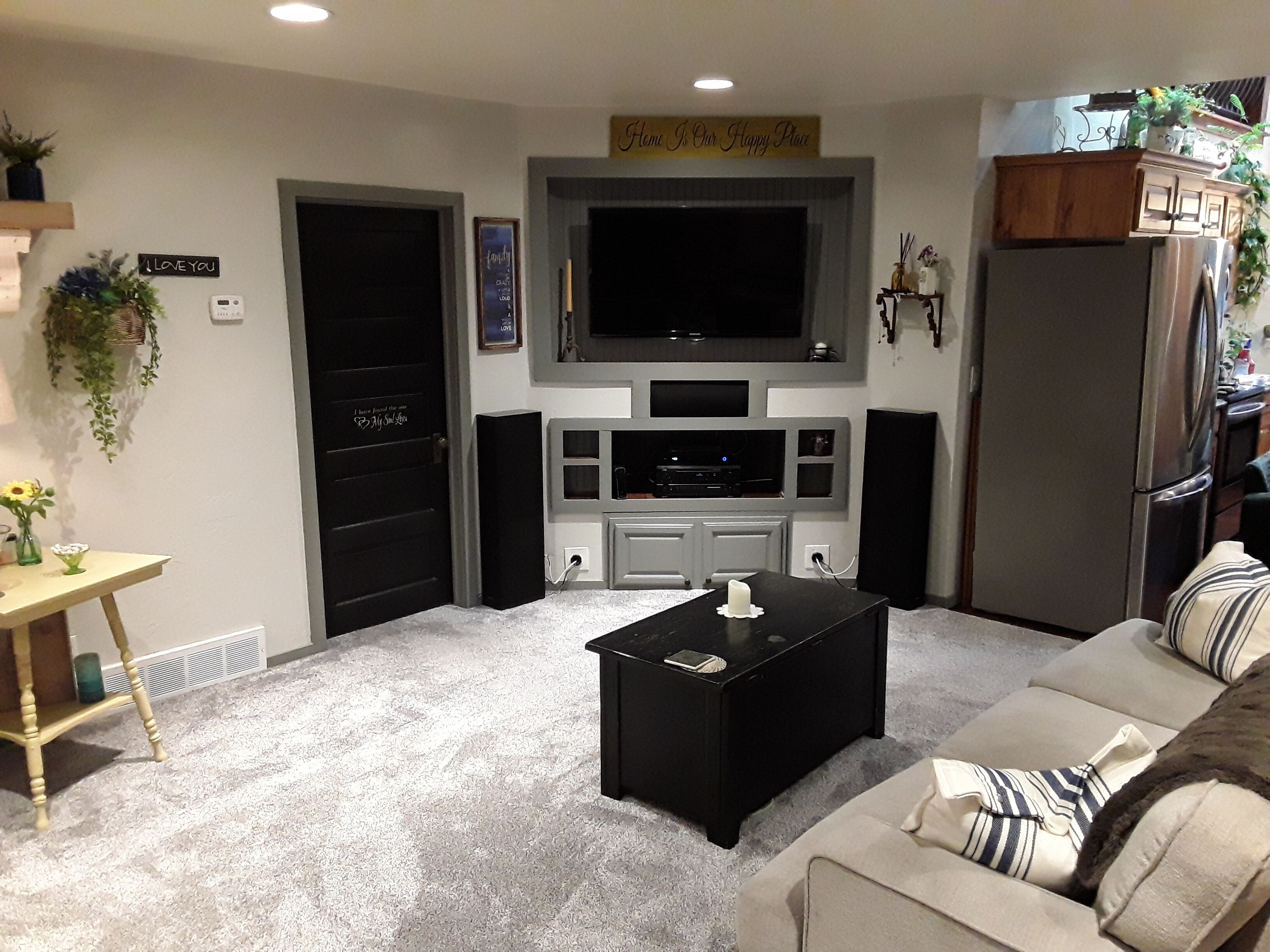 A living room with a flat-screen TV, a black coffee table, a beige sofa, and a small table with a vase.