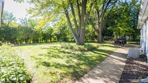 A residential backyard with a lawn, trees, a pathway, and a barbecue area. - Remodeled 3 bedroom home in Monona. Close to Downtown! (Monona)