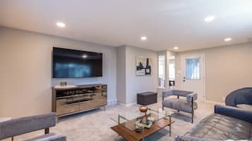 A modern living room with a flat-screen TV, a glass coffee table, and two grey sofas.