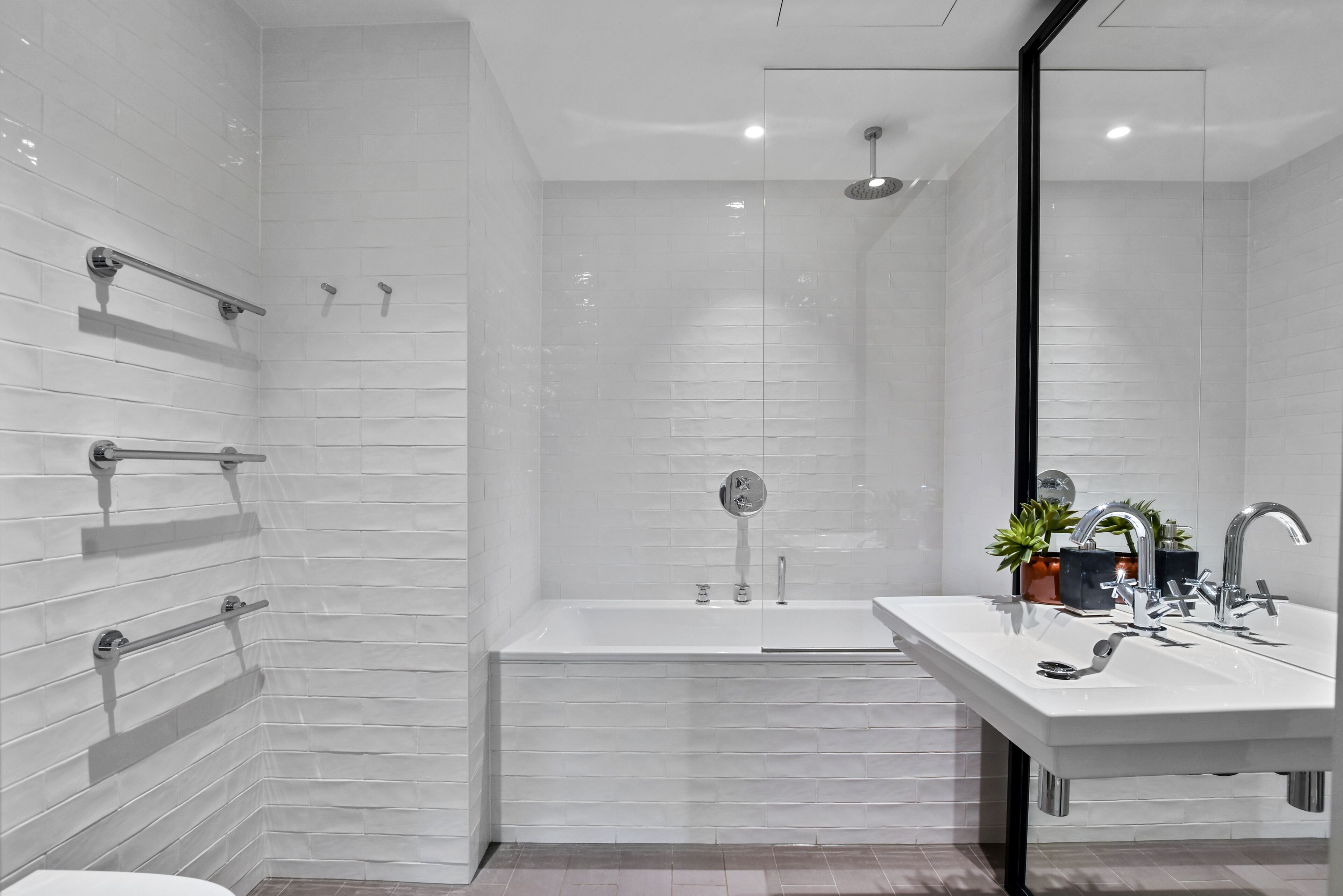 A modern bathroom with a white tiled shower, a bathtub, and a vanity with a sink and mirror.