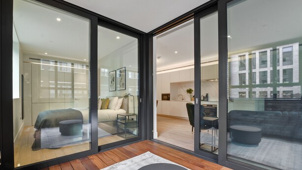 A modern interior with a glass partition, a sofa, a dining area, and a kitchen visible through the glass.