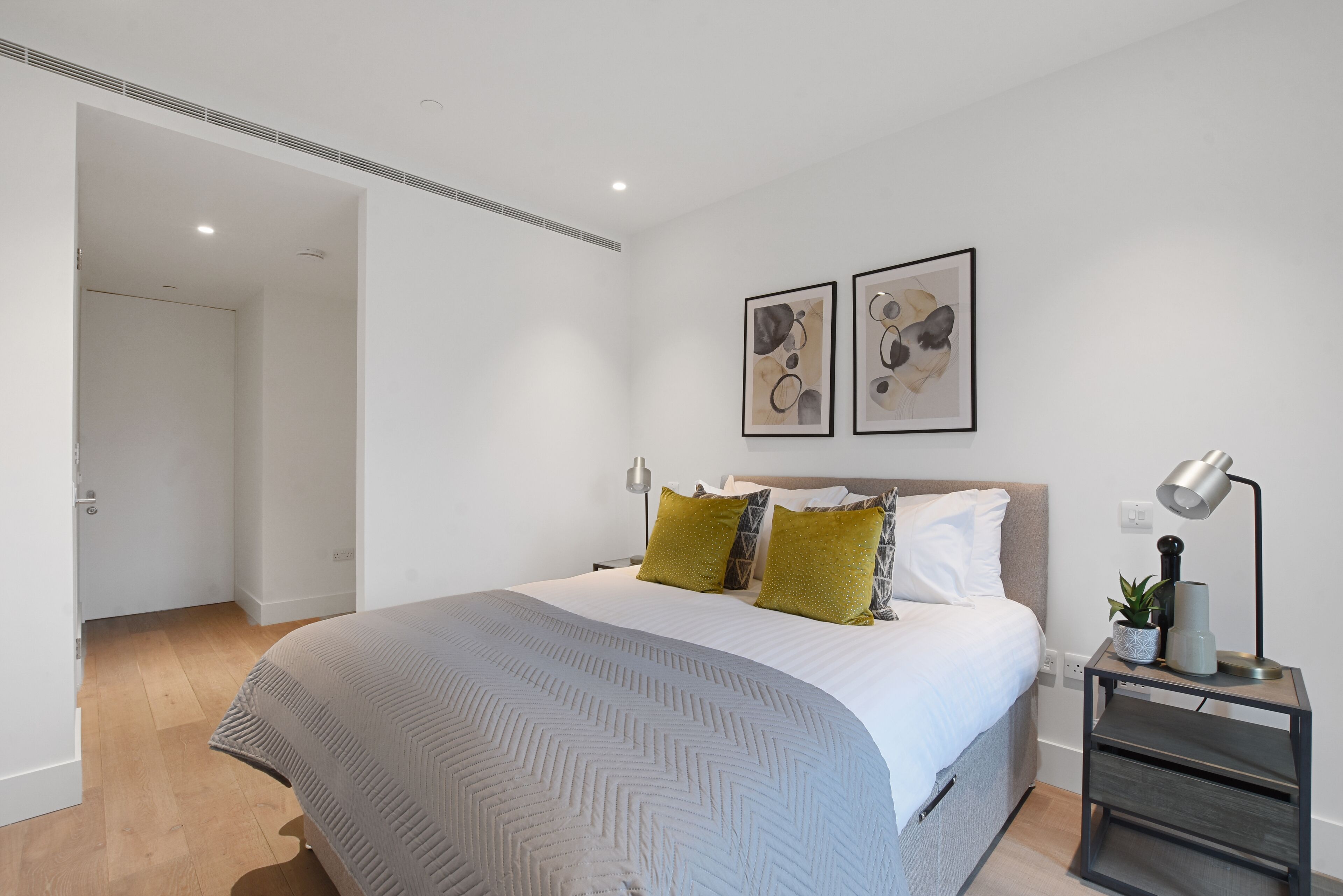 Een moderne slaapkamer met een groot bed, een nachtkastje met een lamp en twee ingelijste kunstwerken aan de muur.