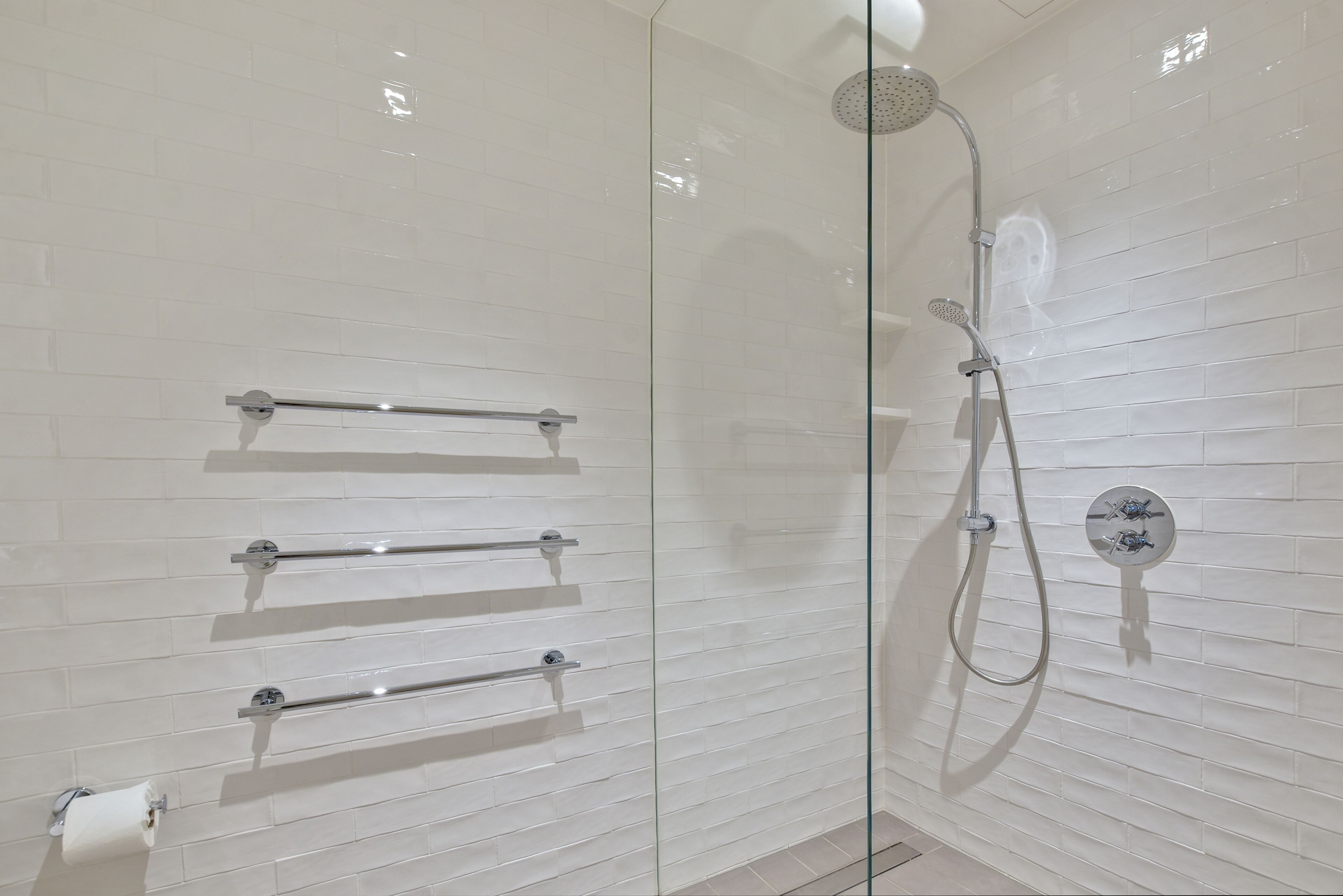 A glass-enclosed shower with a handheld showerhead and a wall-mounted control panel.