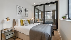 A modern bedroom with a large bed, a nightstand with a lamp, and two framed artworks on the wall.