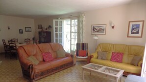 A living room with two sofas, a coffee table, a TV, and a dining area with chairs and a table. - Located in a tranquil woodland setting. (Baladou)