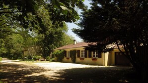 A house with a tiled roof, a front porch, and a small garden area with potted plants. - Located in a tranquil woodland setting. (Baladou)