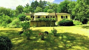 A house with a covered porch, surrounded by lush greenery and a well-maintained lawn. - Located in a tranquil woodland setting. (Baladou)