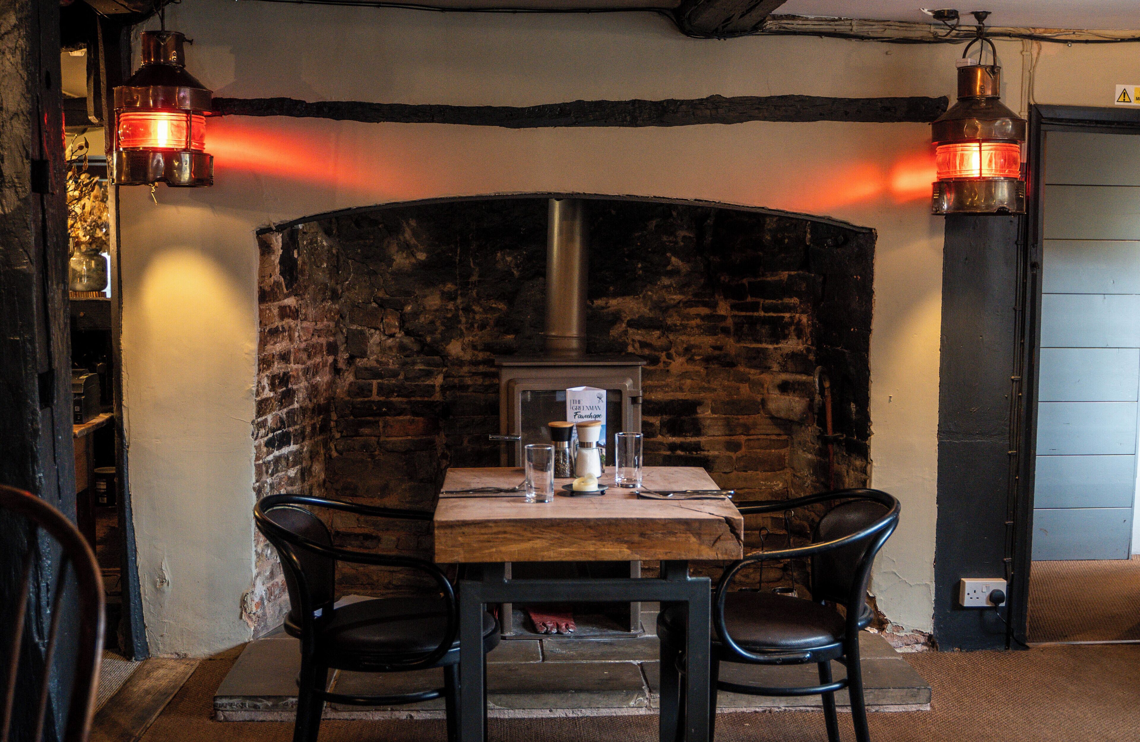 Un interior rústico con chimenea de ladrillo, una mesa de madera y dos sillas.