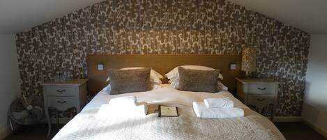 Ein ordentlich bezogenes Bett mit Kopfteil, zwei Nachttischen und einer Wand mit ornamentalem Wandpapier.