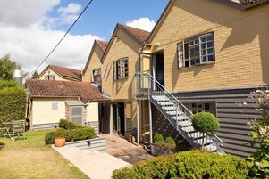 A residential building with a staircase leading to a balcony, a small garden area, and a garage.