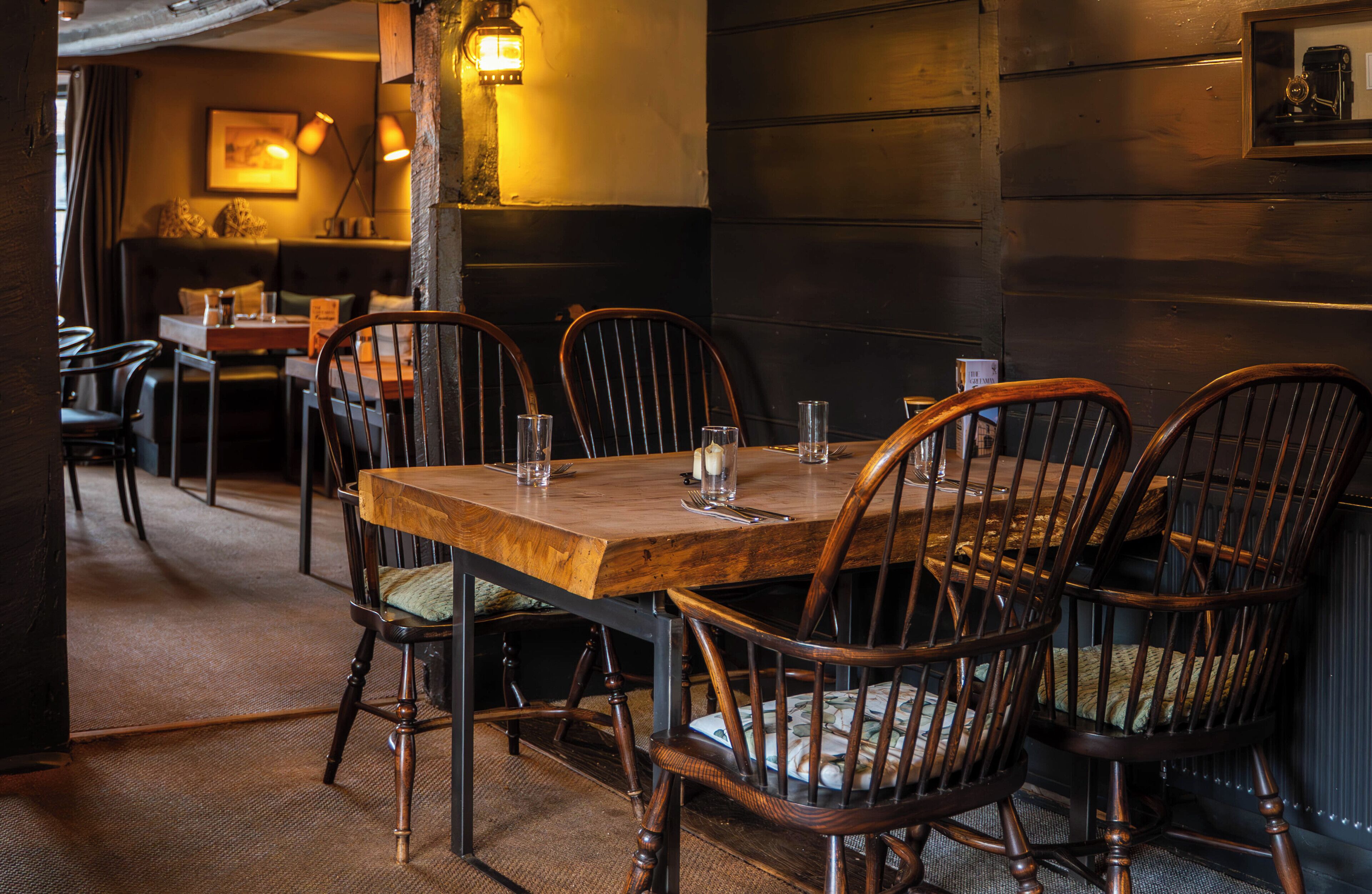 A wooden dining table with chairs, a bench, and a wall-mounted light fixture in a restaurant setting.