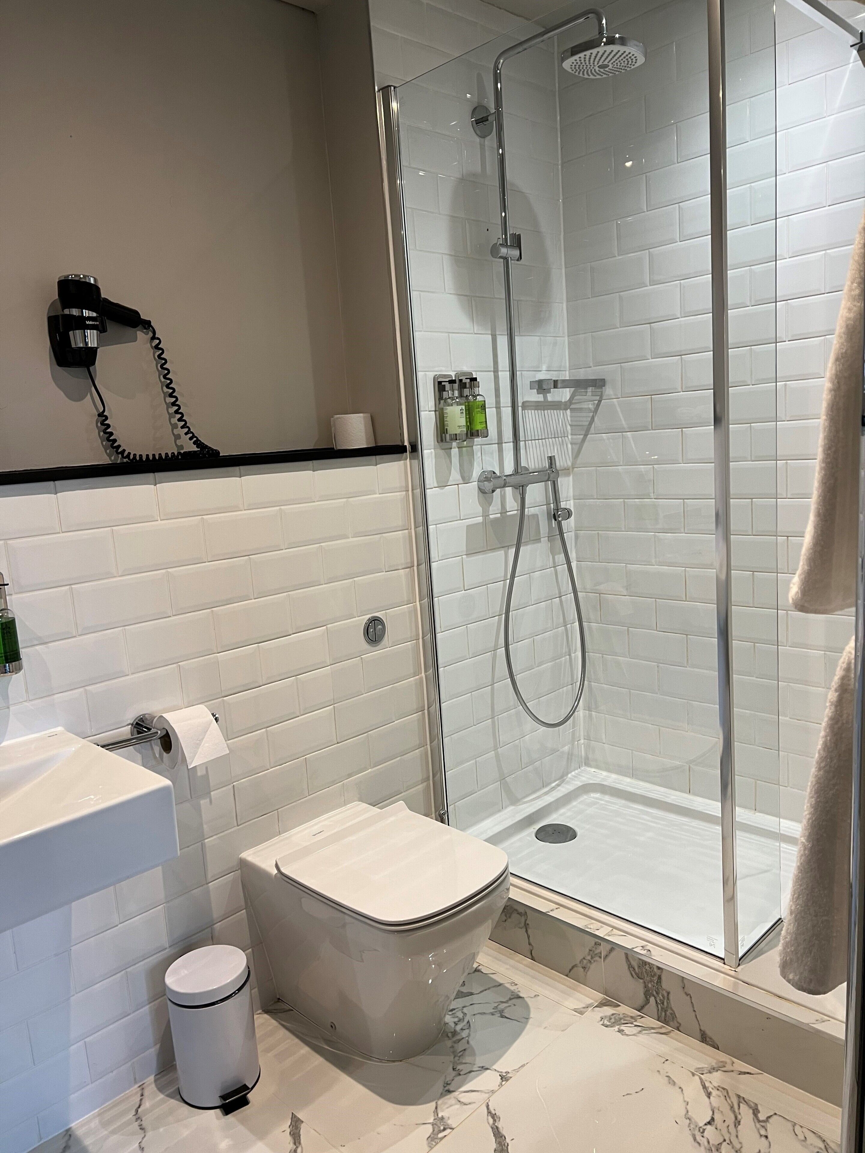 Un baño moderno con ducha de vidrio, inodoro, lavamanos y secador de pelo montado en la pared.