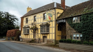 A traditional yellow building with a large window and a mural, located beside a road. - The Green Man (Hereford)