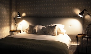 A neatly made bed with a headboard, two bedside lamps, and patterned wallpaper. - The Green Man (Hereford)