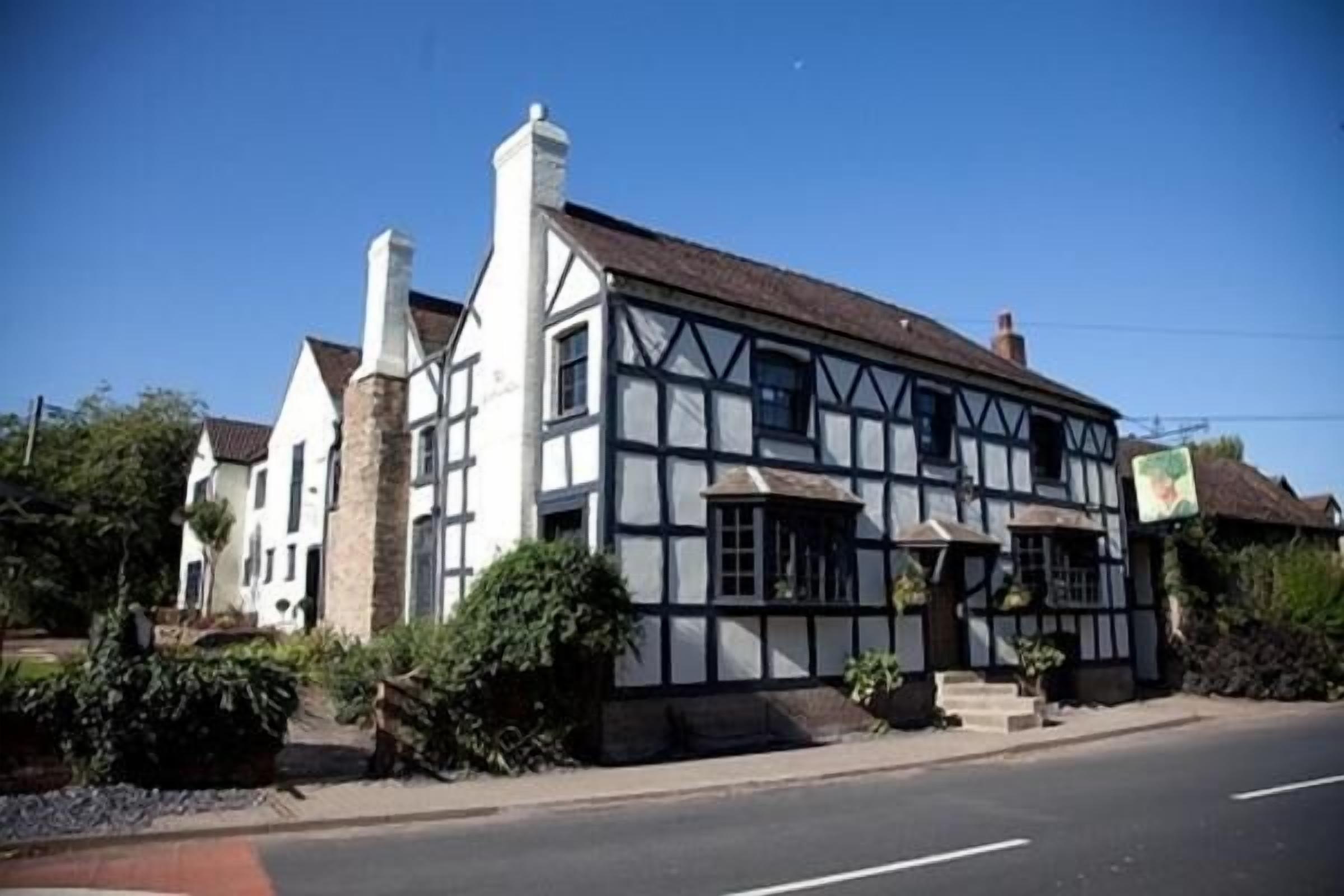 A traditional half-timbered building with a prominent chimney, large windows, and a well-maintained garden.