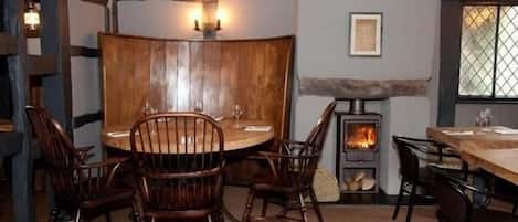 A cozy dining area with a round table and wooden chairs, a stone fireplace, and a window with a view.