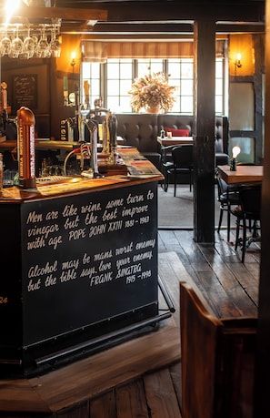 Eine Bar mit einer Tafel, auf der Text steht, verschiedenen Flaschen und Gläsern sowie einer Sitzecke mit einem großen Fenster.