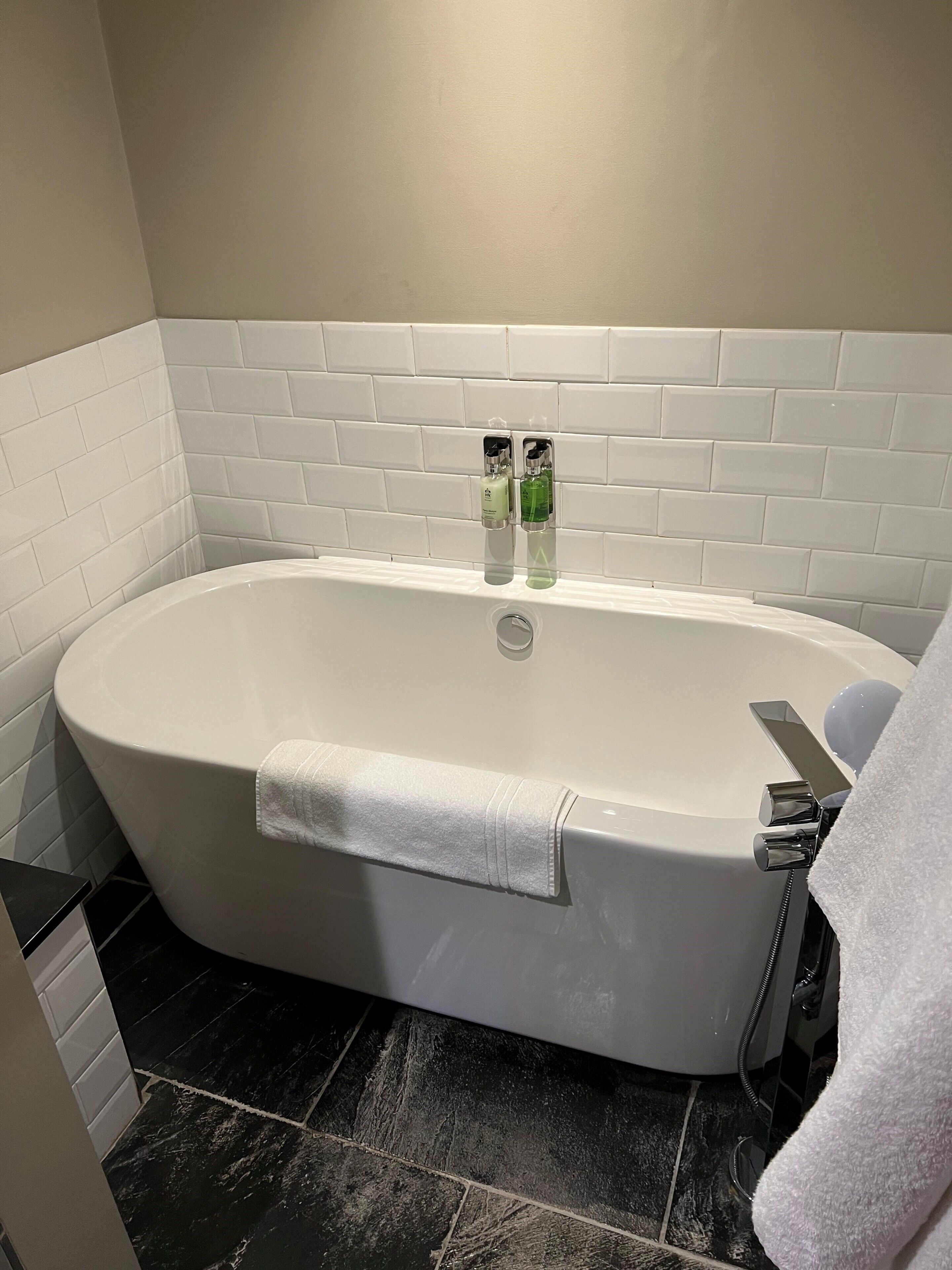 A modern bathroom with a freestanding bathtub, white tiles, and a black tiled floor.