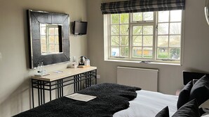 Een slaapkamer met een bed, nachtkastje, spiegel, raam met uitzicht en een radiator.