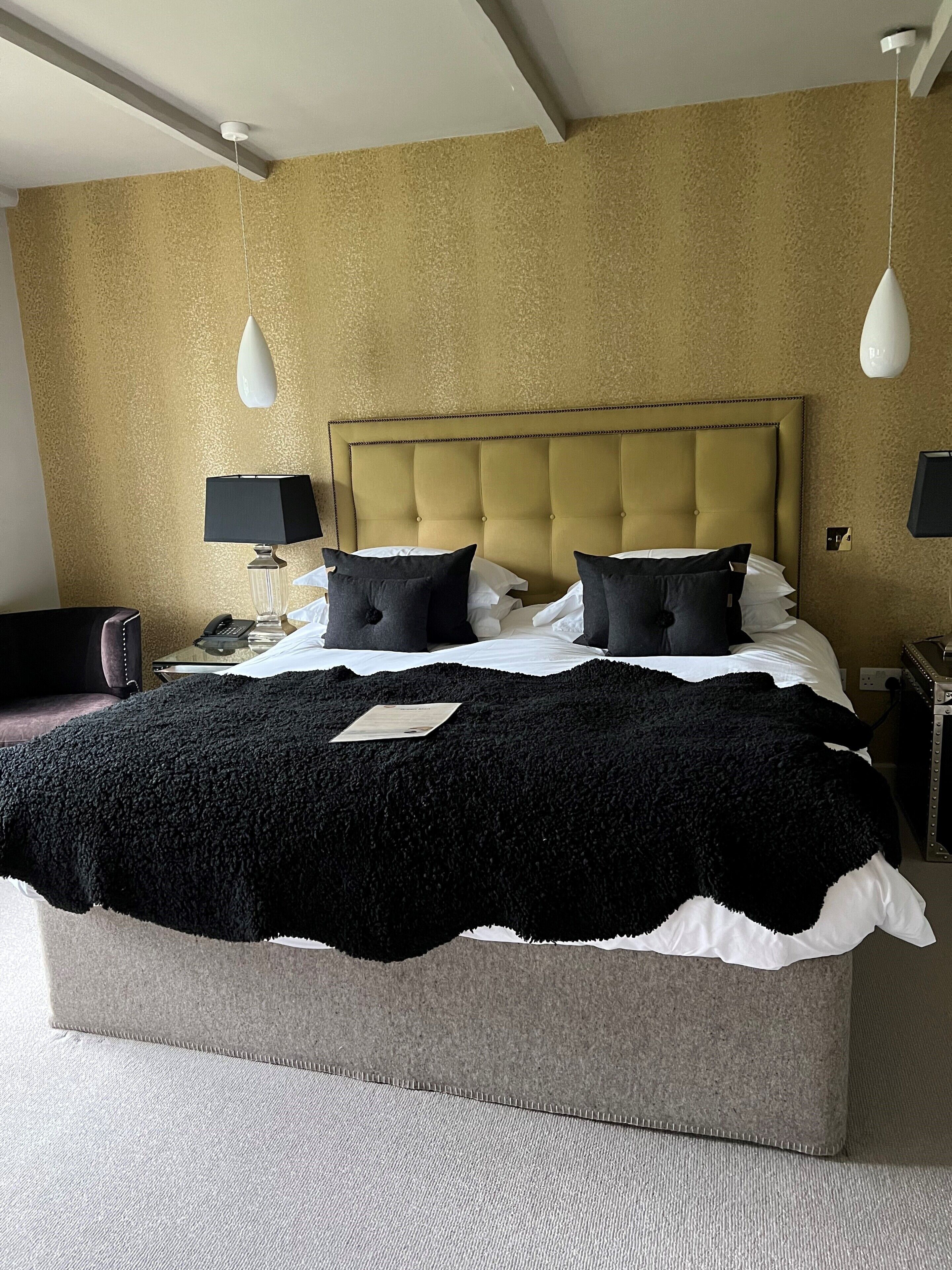 A hotel room with a large bed, a headboard, two bedside lamps, and a carpeted floor.
